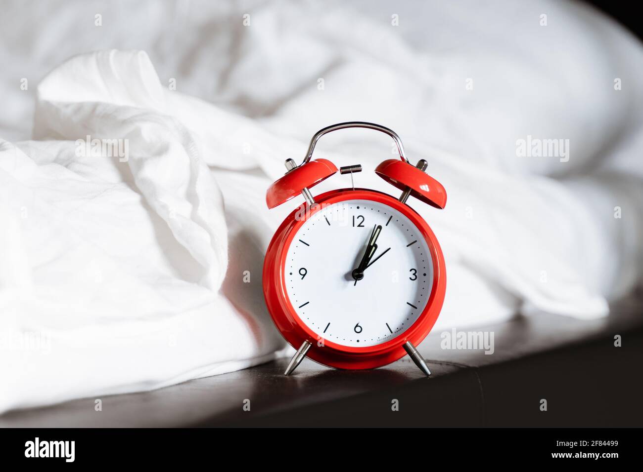 red retro alarm clock near nightstand at bed with white blanket sheet at home in hotel bedroom