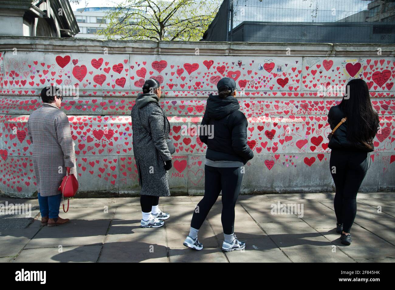 Southbank, London, England, UK. National Covid Memorial Wall. A group of young people look at the red hearts to commerate those who died of Covid. Stock Photo