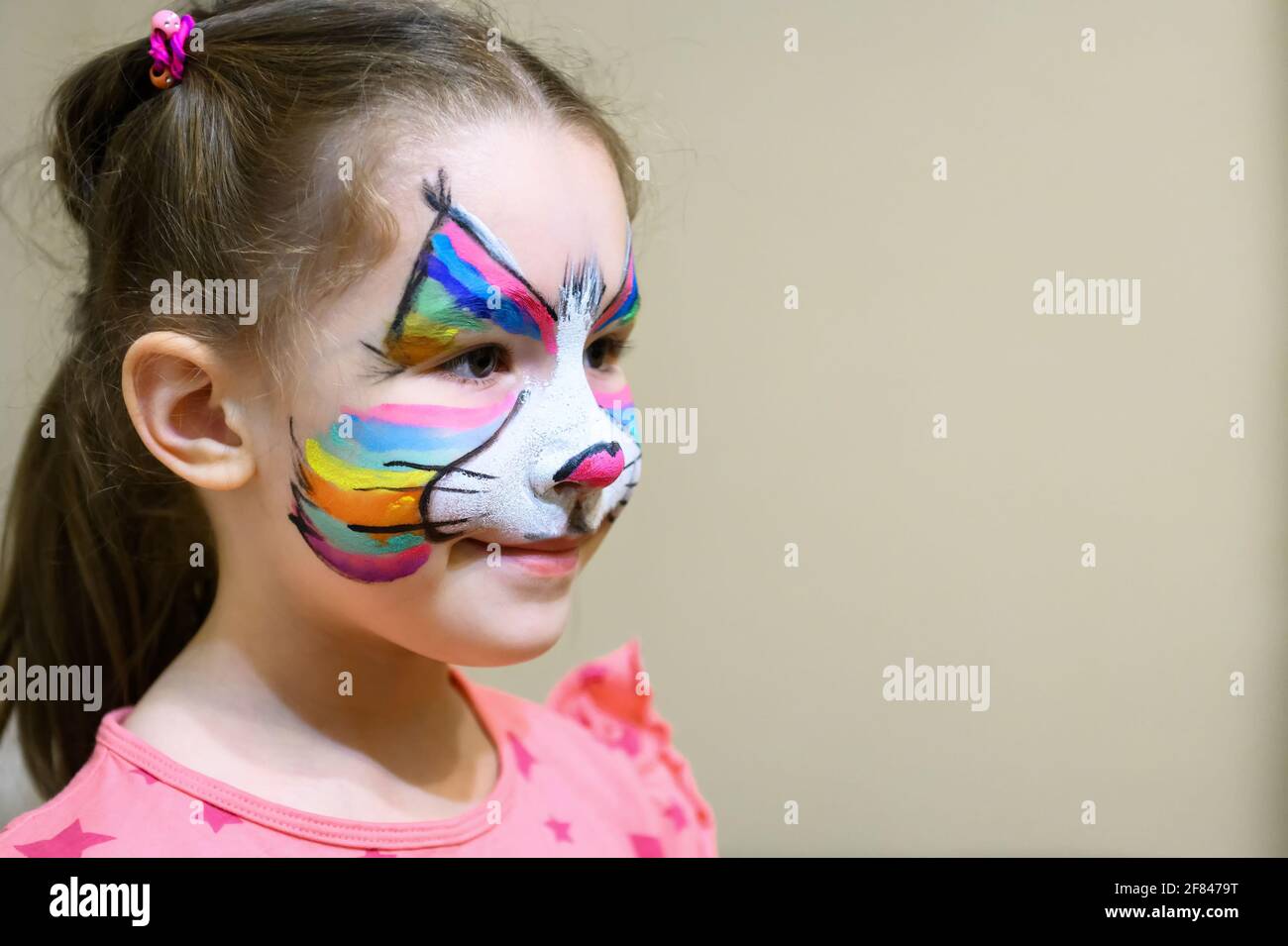 Kid with face painting of kitty, cute little girl with painted mask on face of rainbow cat. Portrait of pretty child with beautiful makeup and copy sp Stock Photo