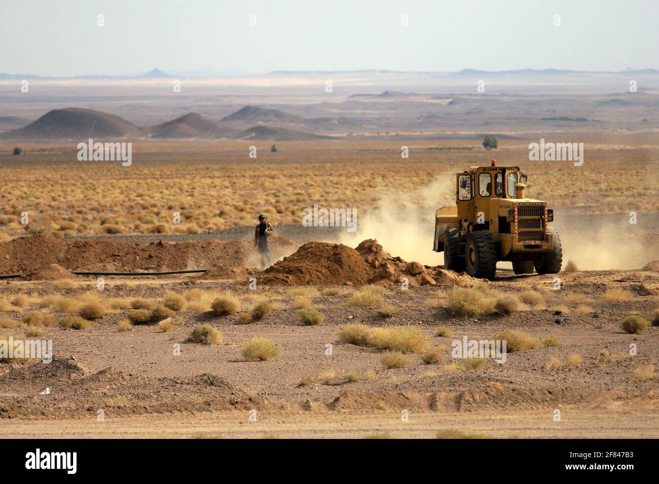 Straßenbau in der Wüste Lut. Nur wenige Hügel stehen dem Blick bis zum Horizont im Wege. Stock Photo