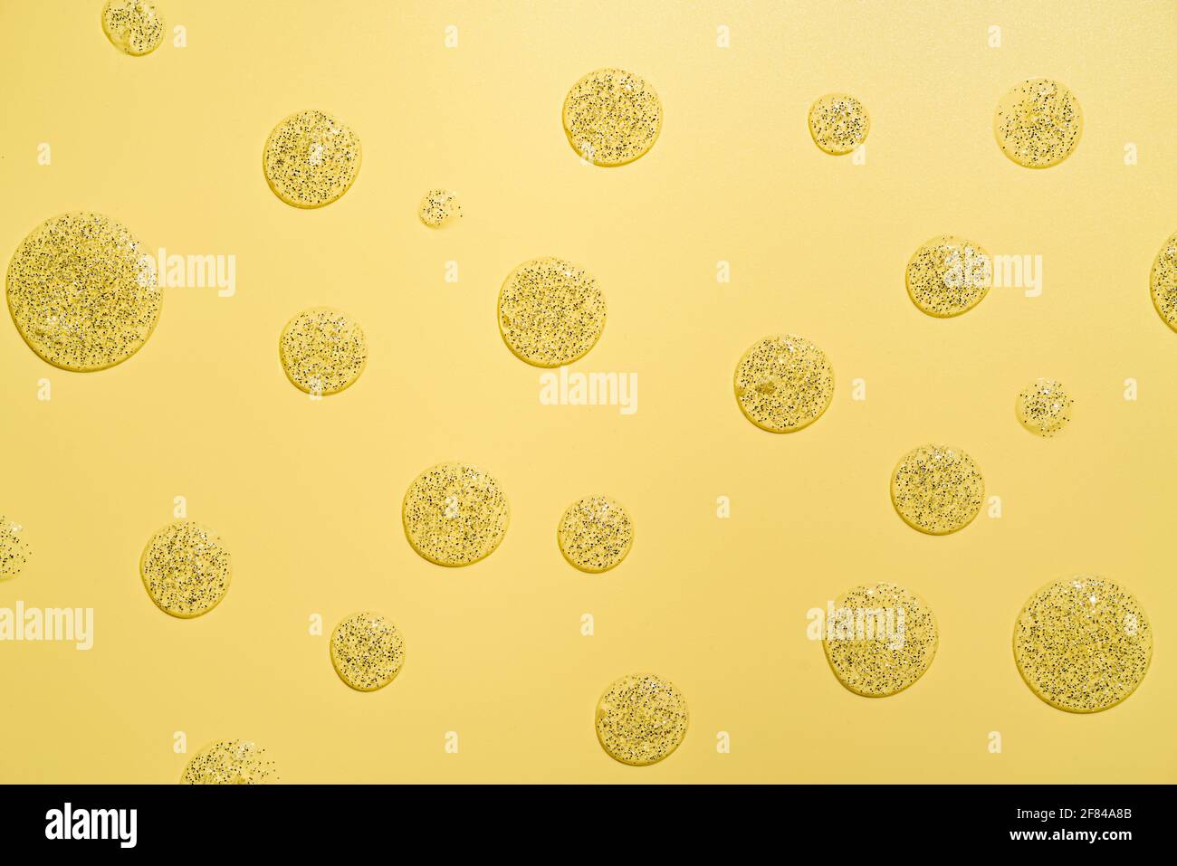 Yellow background with cosmetic lotion or transparent gel drops and smears with glitter Stock Photo