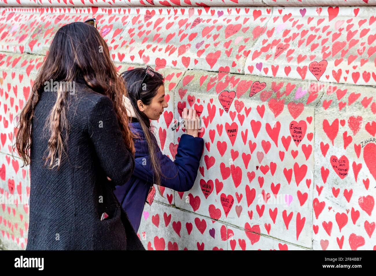 11 April 2021, London, UK - Woman signing The National COVID Memorial Wall on the South Bank which has hearts drawn and names of those who died in the coronavirus pandemic Stock Photo