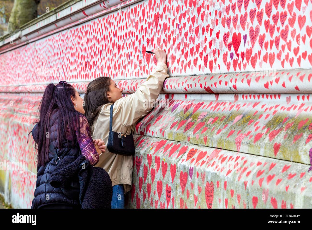 11 April 2021, London, UK - Woman signing The National COVID Memorial Wall on the South Bank which has hearts drawn and names of those who died in the coronavirus pandemic Stock Photo