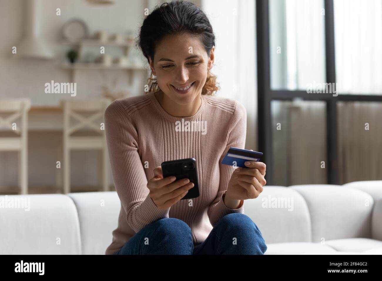 Smiling latina lady holding phone bank card make online shopping Stock Photo