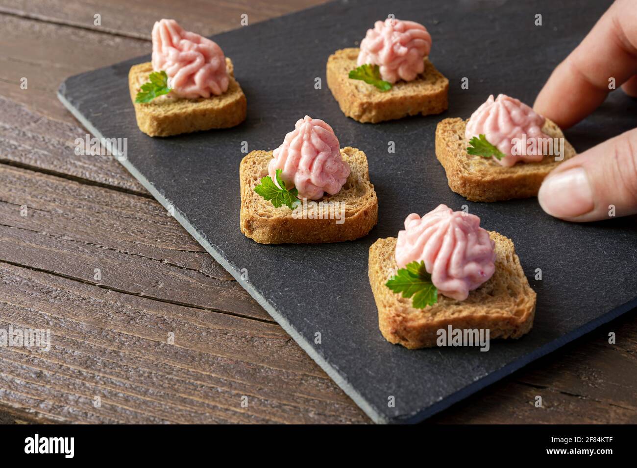 Hand takes crostini or canapes with taramasalata from a slate board Stock Photo