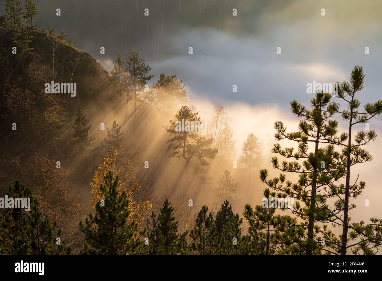 Dramatic scene of sun rays braking mist and clouds on a mountain peak Stock Photo