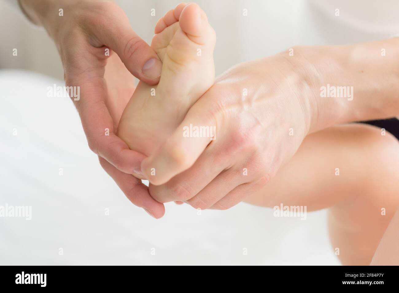 Mom gives her baby a leg and foot massage. Close-up. A satisfied baby lies on the massage table. Stock Photo