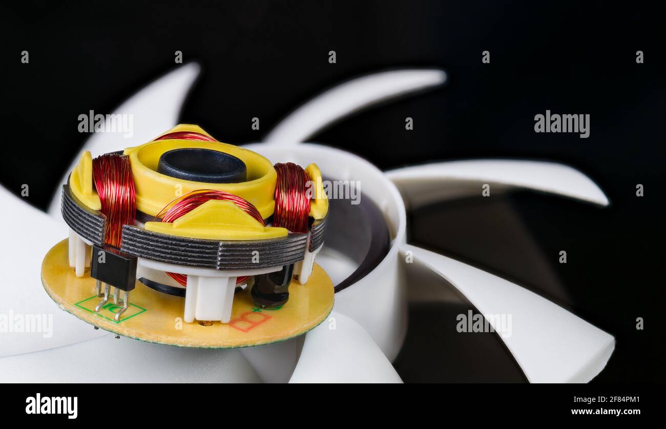 Closeup of rotor and stator from open electric EC motor in computer fan with white plastic blades. Red copper wire coils and iron ferromagnetic sheets. Stock Photo