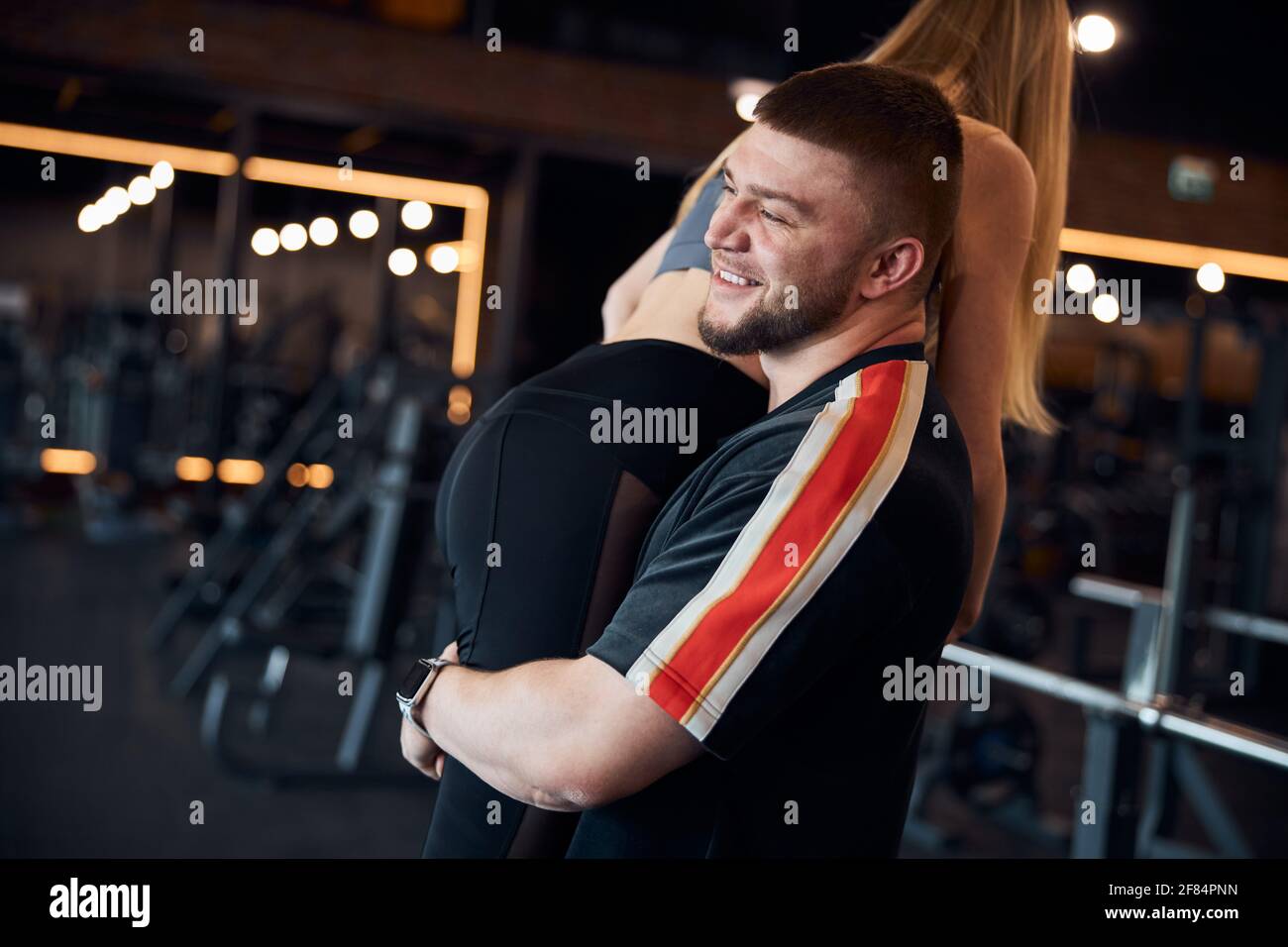 Smiley young man carrying a woman in sports attire Stock Photo