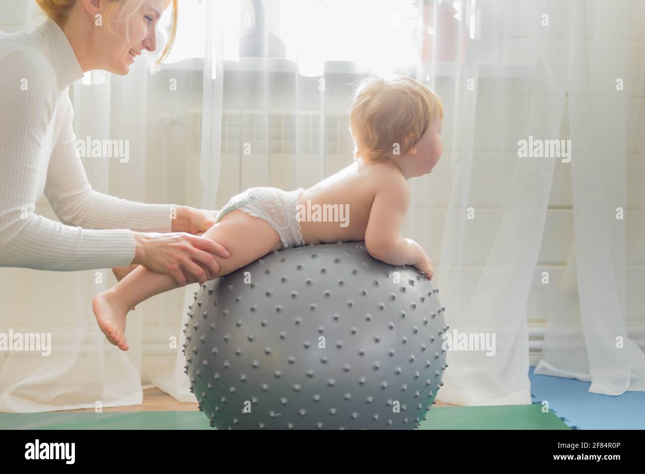 Mom is engaged in gymnastics with the baby on an inflatable ball. Fitball, gymnastics for a child. Stock Photo
