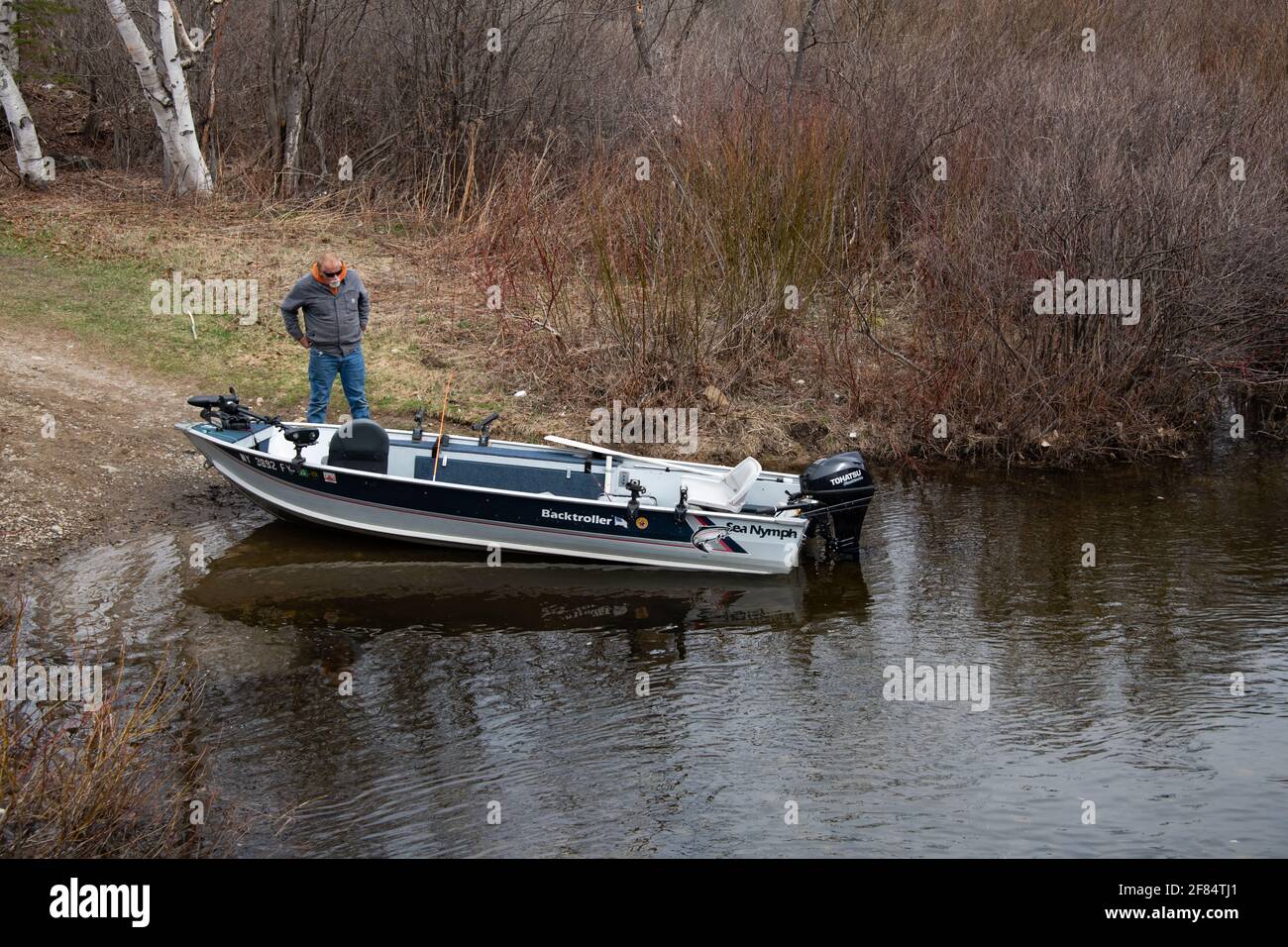 Man looking at aluminum outboard fishing boat on the Sacandaga River at the outlet of Lake Pleasant in Speculator, NY USA in the Adirondack Mountains. Stock Photo