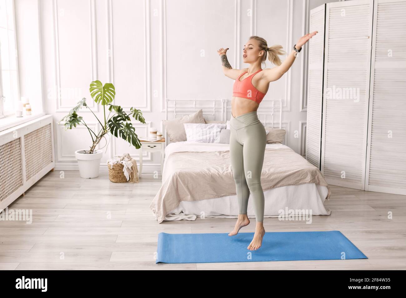 Sportive beautiful woman exercise at home, doing jumping jacks. Happy blonde-hair female fitness trainer is working out, smiling, healthy lifestyle Stock Photo