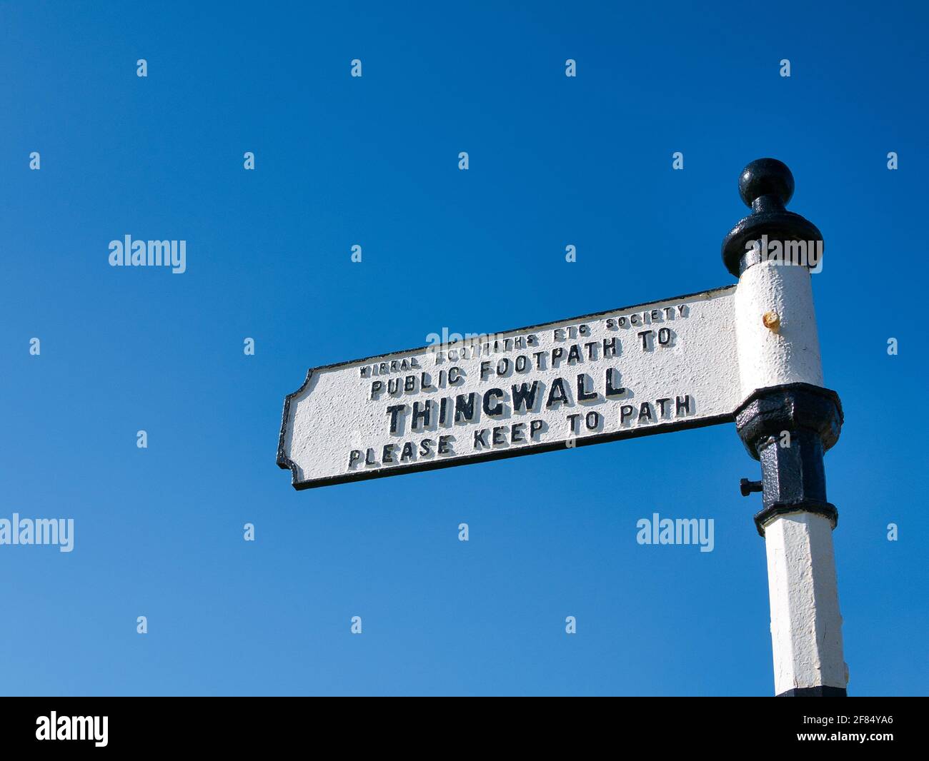 Isolated against a clear blue sky, a white metal sign shows the way on a footpath from Storeton to Thingwall on Wirral in the UK Stock Photo