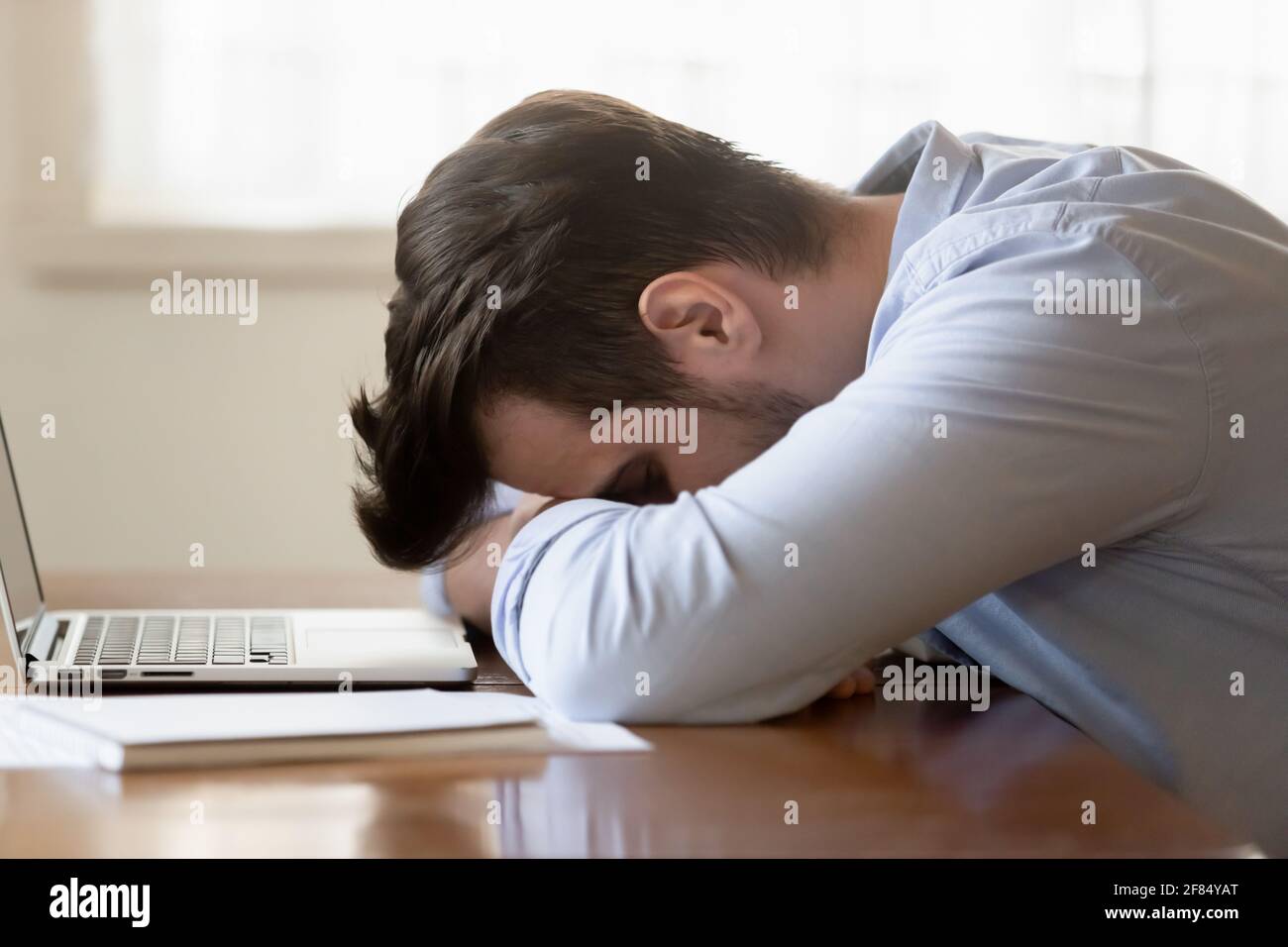 Tired young man fall asleep on table working on laptop Stock Photo