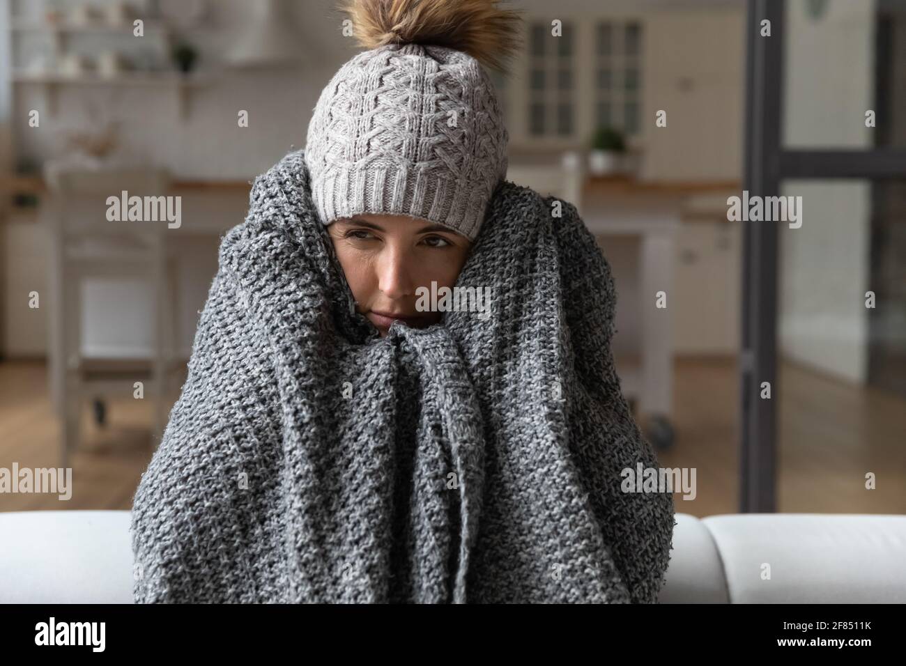 Shivering young lady feel cold sit on sofa in plaid Stock Photo