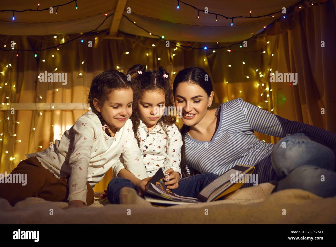 Mother with daughters children reading book spending time in home tent Stock Photo