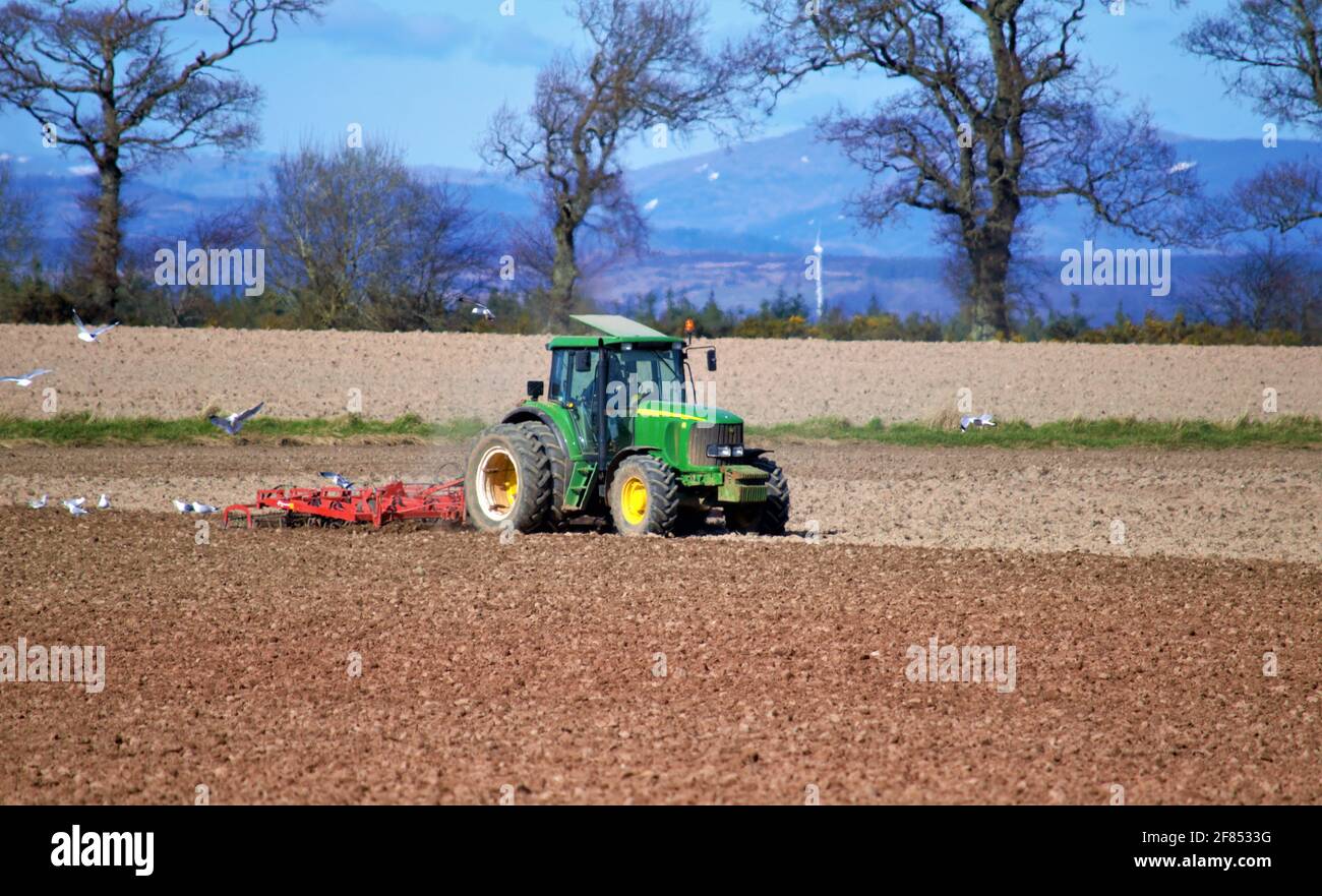 John Deere tractor cultivating field in preparation for cereal crop sowing Stock Photo