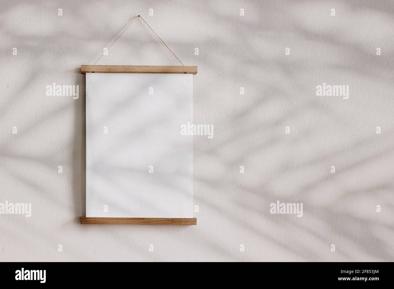 Blank wooden picture frame hanging on beige wall. Empty poster mockup for art display in sunlight. Minimal interior design.Palm leaves shadow overlay Stock Photo