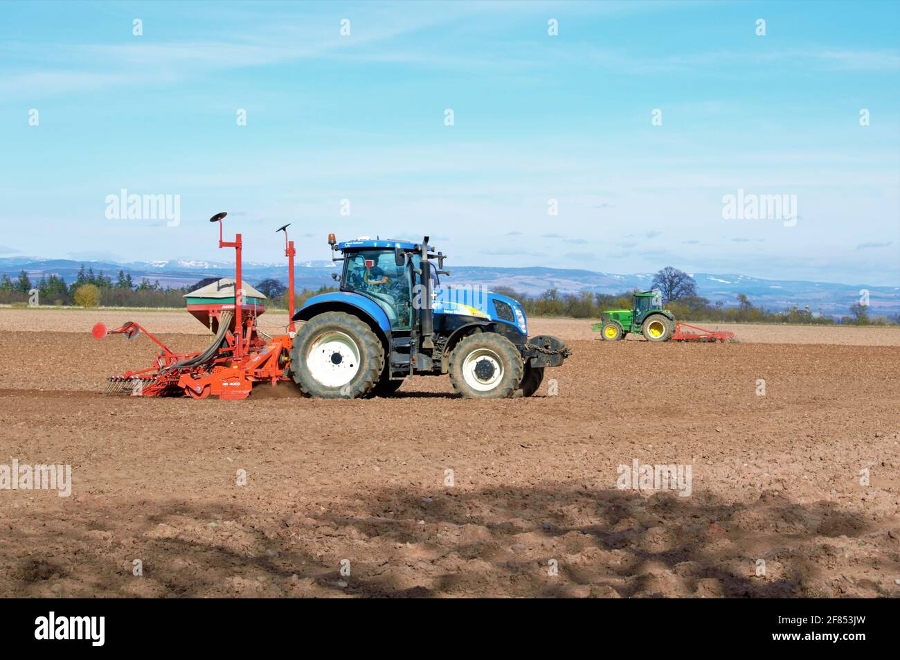 New Holland tractor sowing cereal crop with 1 pass drill under a blue sky Stock Photo