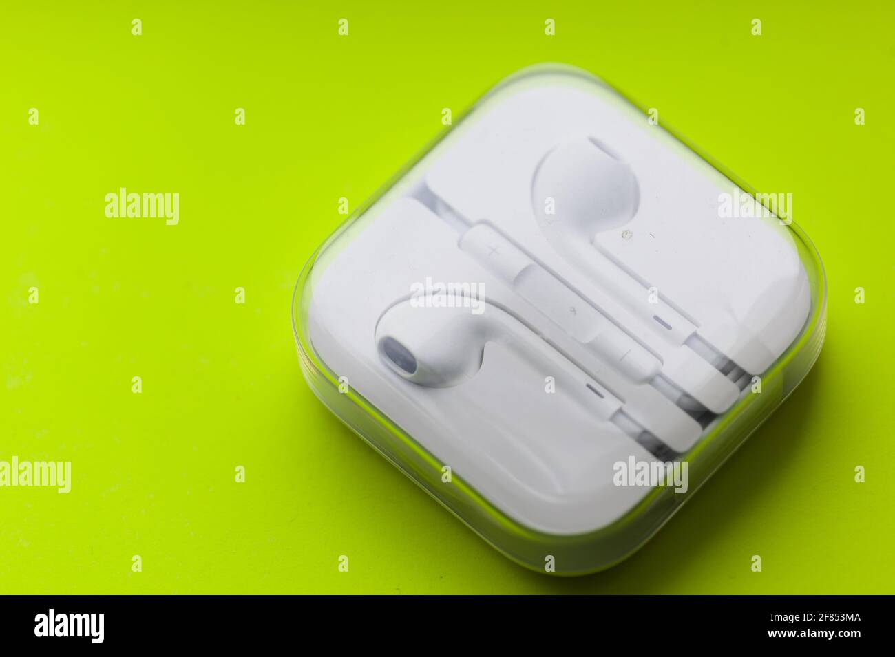 Wearable Tech / Lifestyle - Close-up of a pair of boxed earpod headphones on a neon yellow background Stock Photo