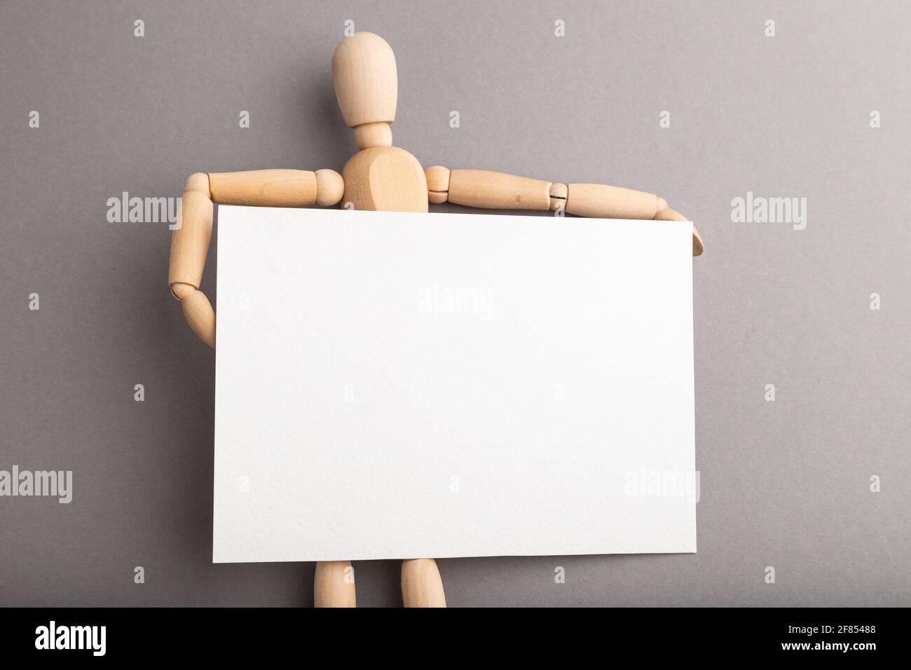 Wooden mannequin holding blank poster on gray pastel background. copy