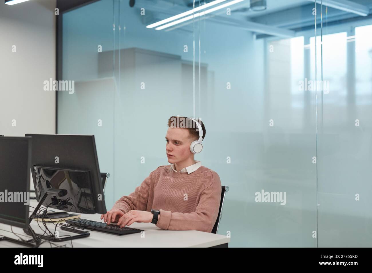 Portrait of young man using computer while working in IT lab or office ...