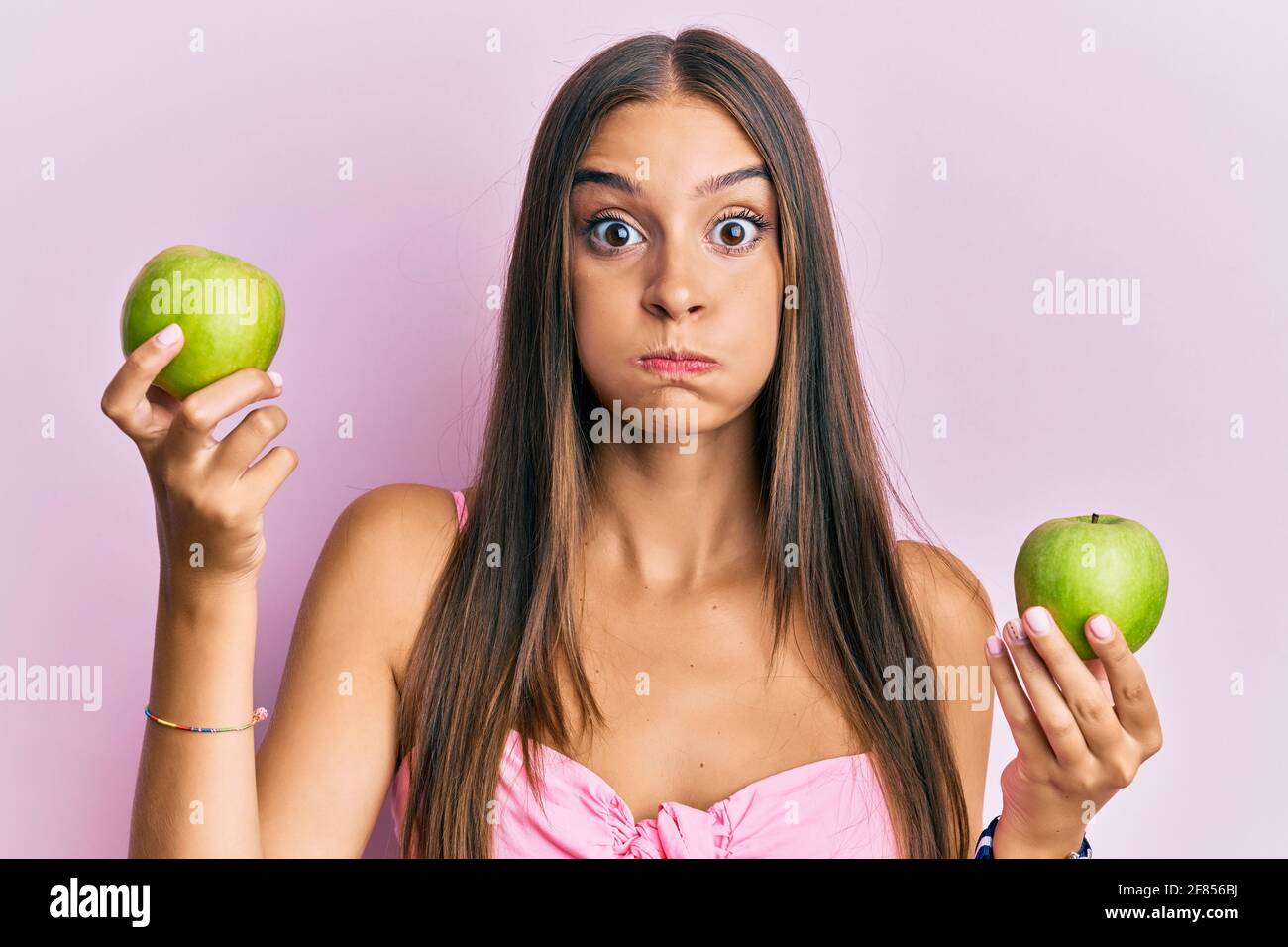 Young Hispanic Woman Holding Green Apples Puffing Cheeks With Funny 