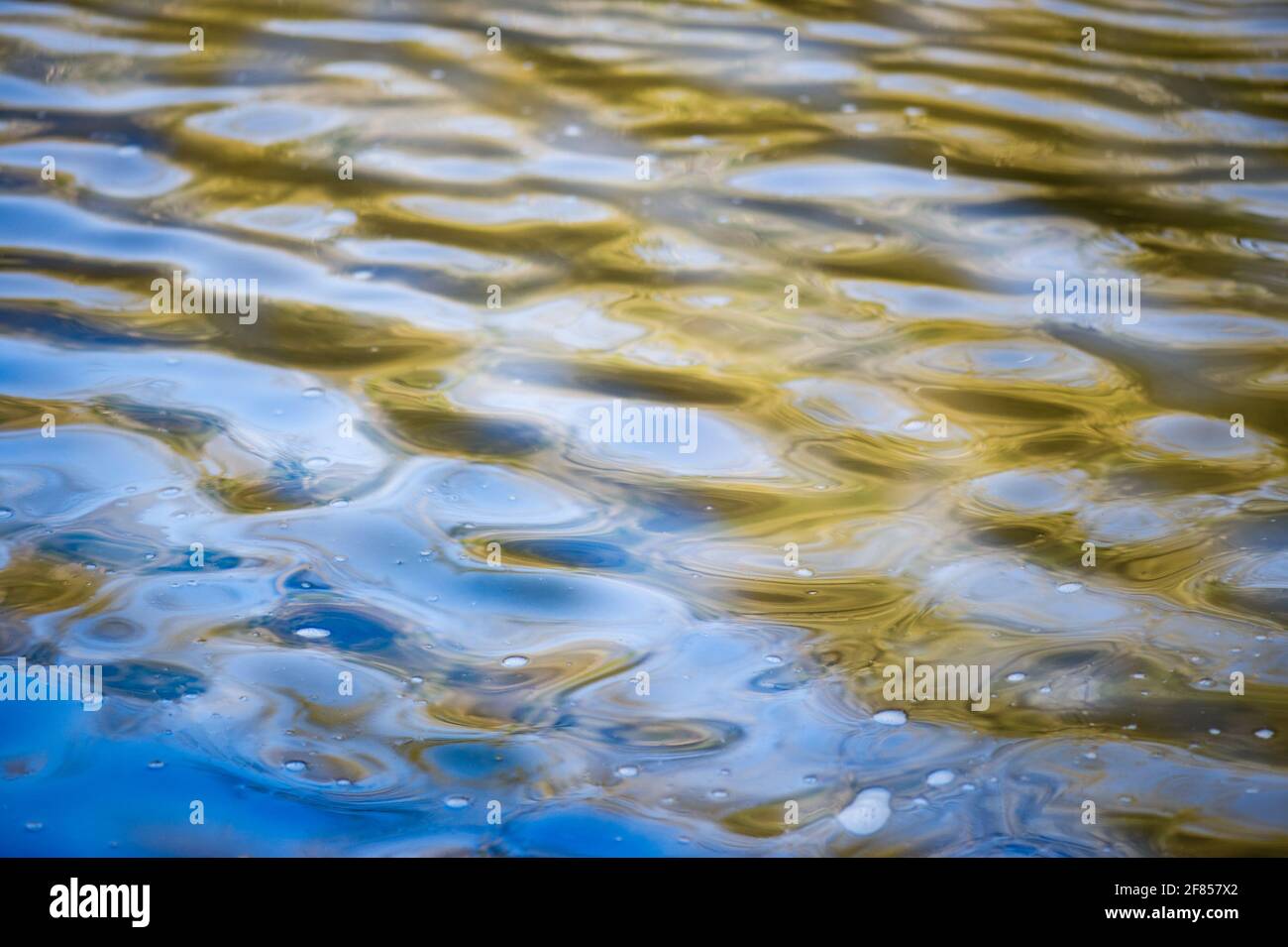 Abstract closeup image of water ripples and reflections in a gently flowing river on a hazy, breezy sunny day. Stock Photo