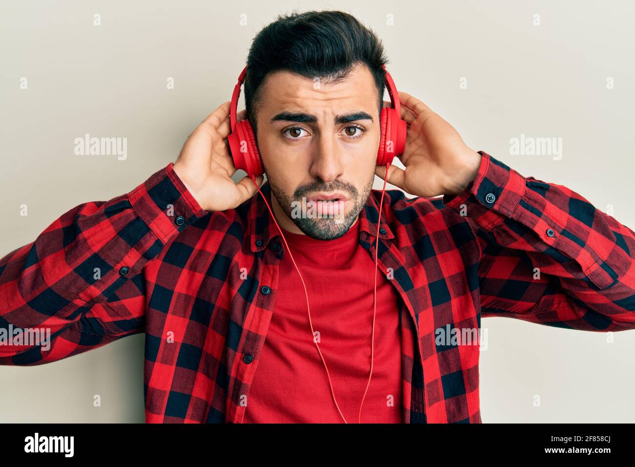 Confusing Music Young hispanic man listening to music using headphones clueless and ...
