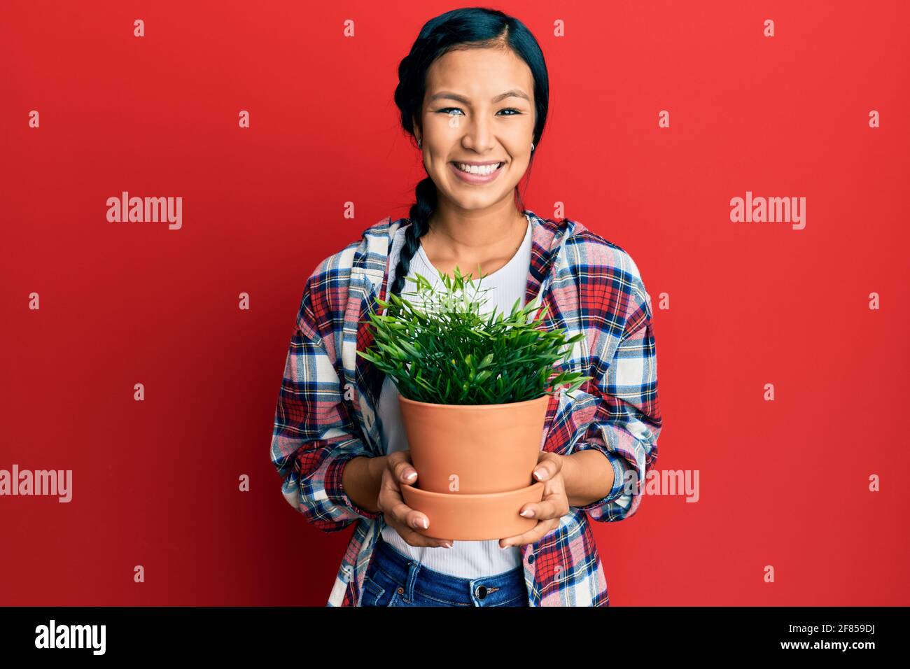Beautiful hispanic woman wearing gardener shirt holding plant pot ...