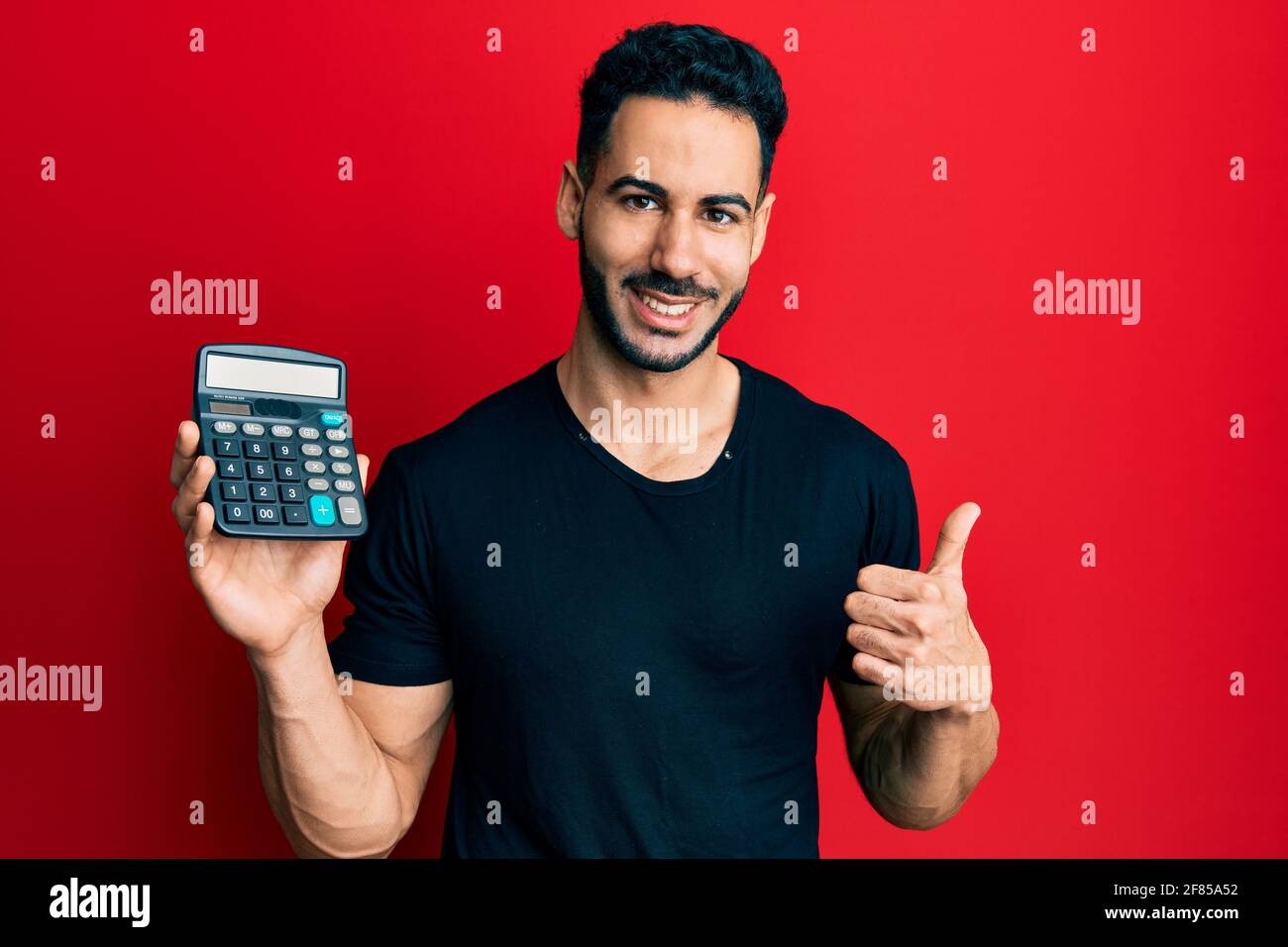 Young hispanic man showing calculator device smiling happy and positive ...