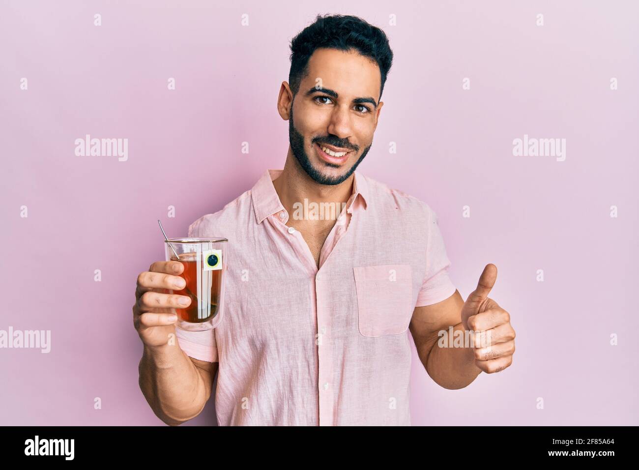 Young hispanic man holding cup of tea smiling happy and positive, thumb ...
