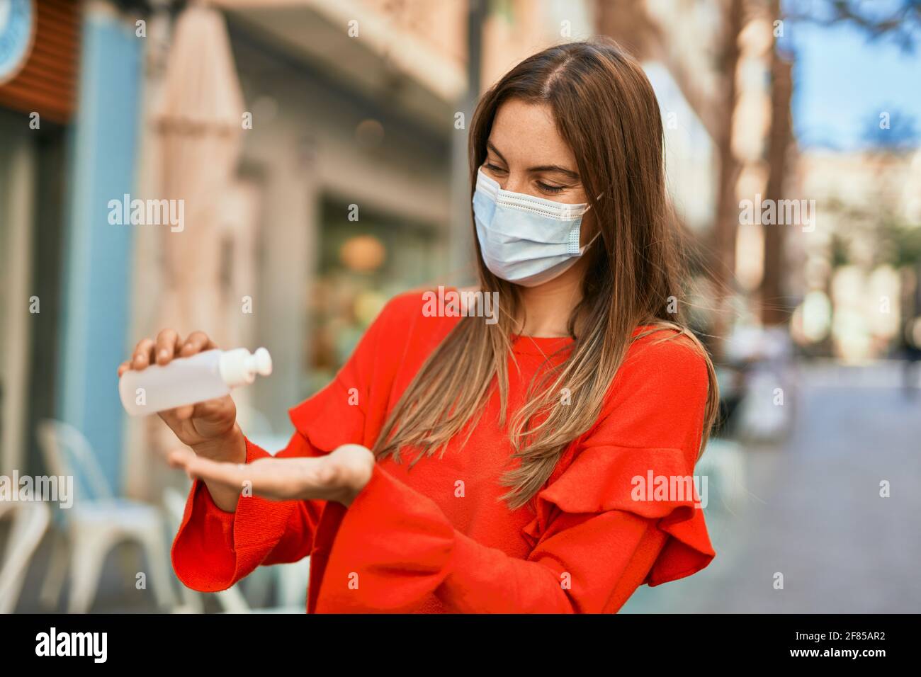 Young hispanic woman wearing medical mask and using hand sanitizer gel ...