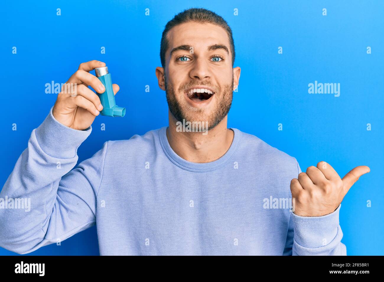 Young caucasian man holding medical asthma inhaler pointing thumb up to ...