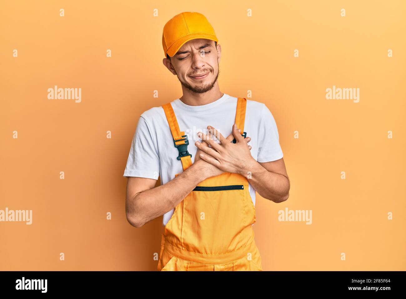 Hispanic young man wearing handyman uniform smiling with hands on chest ...