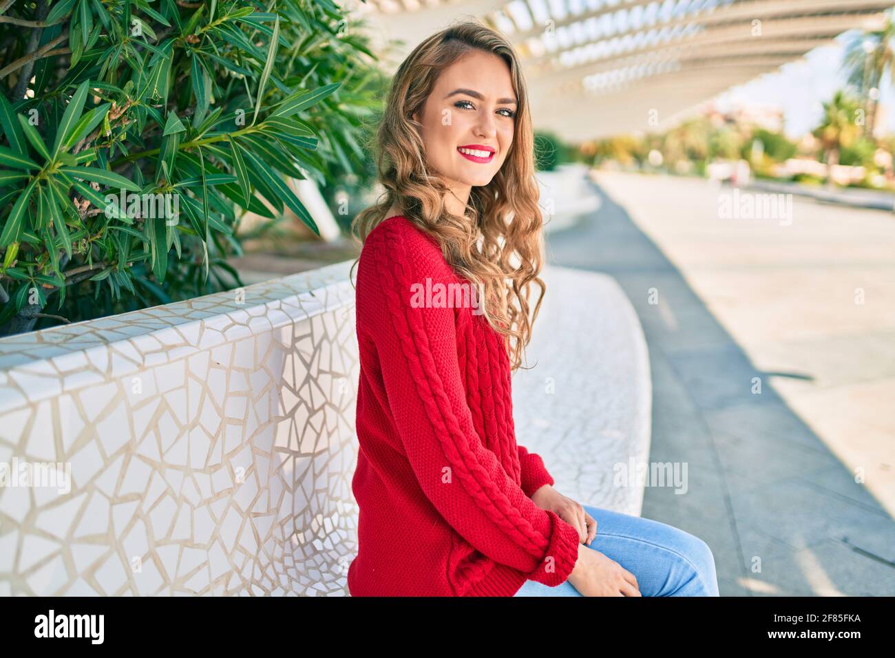 Young blonde girl smiling happy sitting on the bench at the park Stock ...