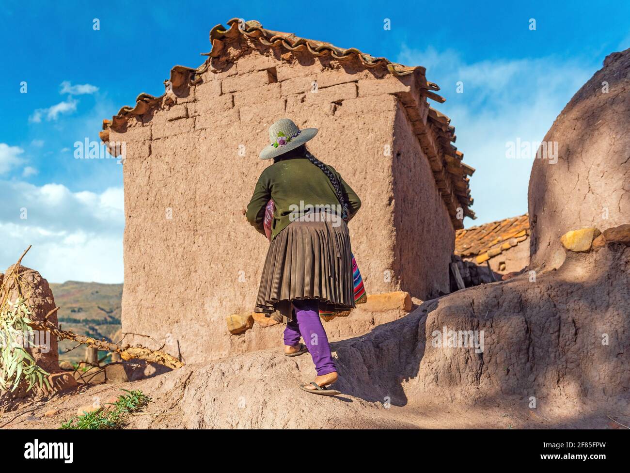 Bolivian Jalq'a indigenous woman in traditional clothing walking to her adobe house, Potolo, Sucre department, Bolivia. Stock Photo