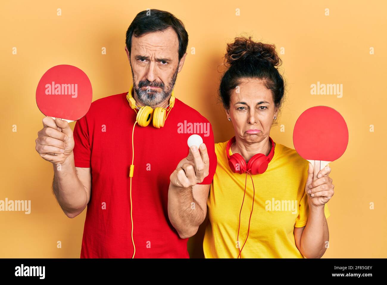 Middle age couple of hispanic woman and man holding red ping pong rackets depressed and worry for distress, crying angry and afraid. sad expression. Stock Photo