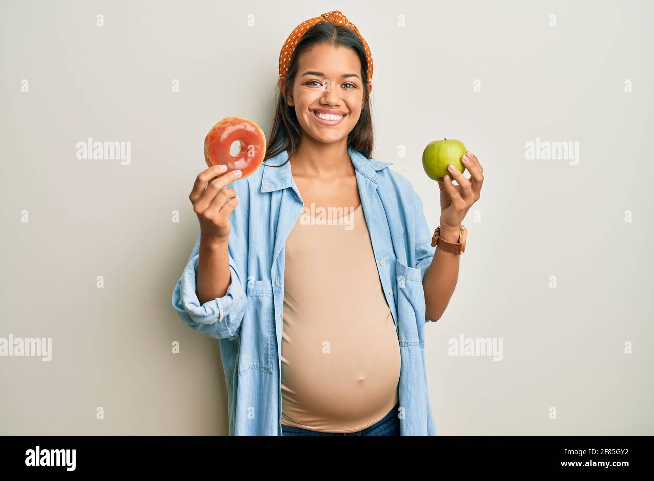 Beautiful hispanic woman expecting a baby, holding food smiling with a happy and cool smile on face. showing teeth. Stock Photo