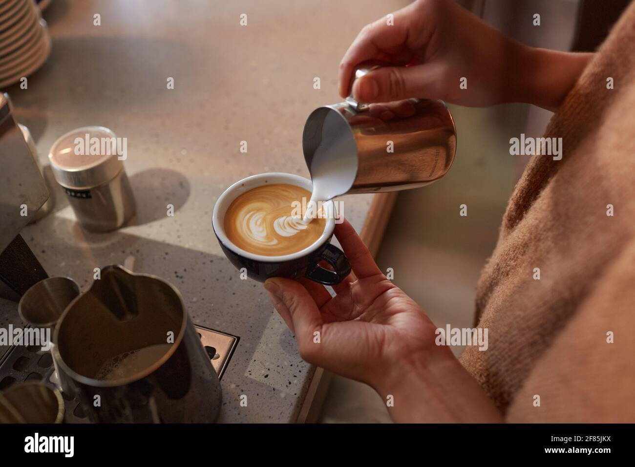 Close up of unrecognizable barista creating latte art with cream while making fresh coffee in cafe or coffee shop, copy space Stock Photo