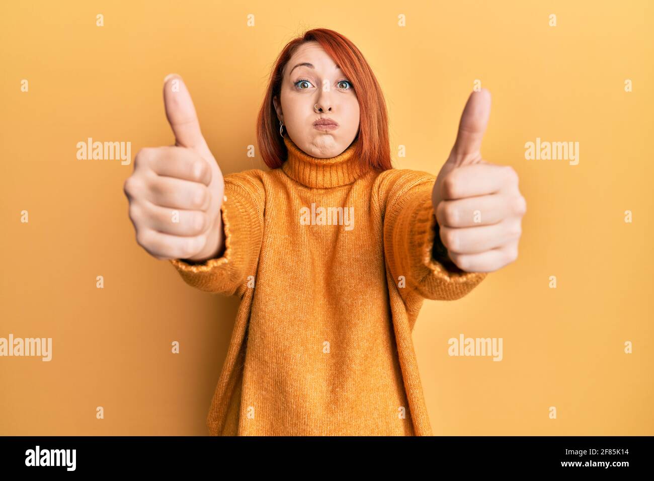 Beautiful redhead woman doing thumbs up positive gesture puffing cheeks with funny face. mouth inflated with air, catching air. Stock Photo