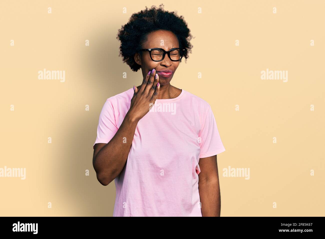 African american woman with afro hair wearing casual clothes and glasses touching mouth with hand with painful expression because of toothache or dent Stock Photo