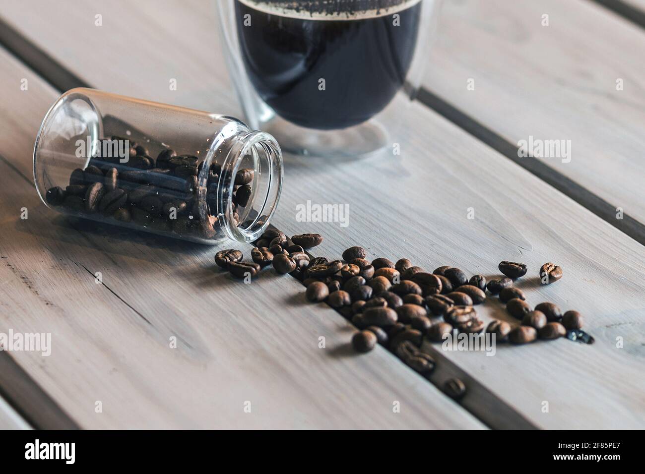 Transparent glass cup of hot coffee and coffee beans on wooden table. Stock Photo