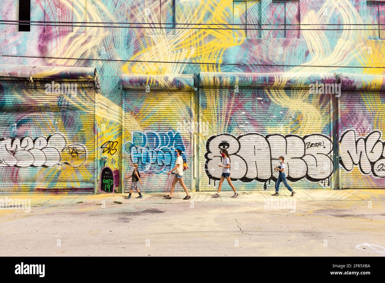 A sightseeing family walks down a street with colorful street art covering every wall in sight in the Wynwood Art District, Miami, FLorida, USA Stock Photo
