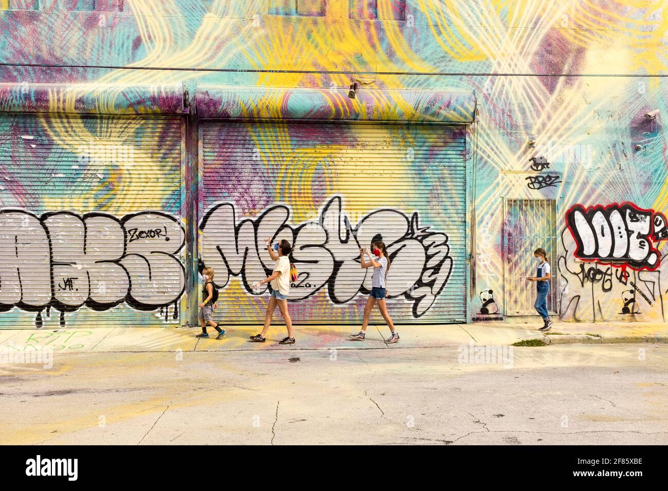 A family walks down a street looking at  street art covering every wall in sight in the Wynwood Art District, Miami, FLorida, USA Stock Photo