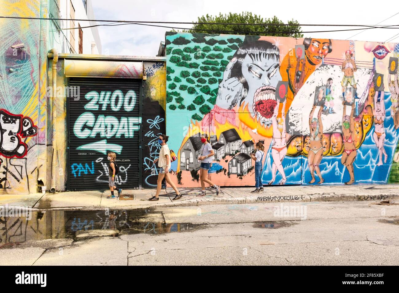 A family of tourists walks down a street with street art covering every wall in sight in the Wynwood Art District, Miami, FLorida, USA Stock Photo