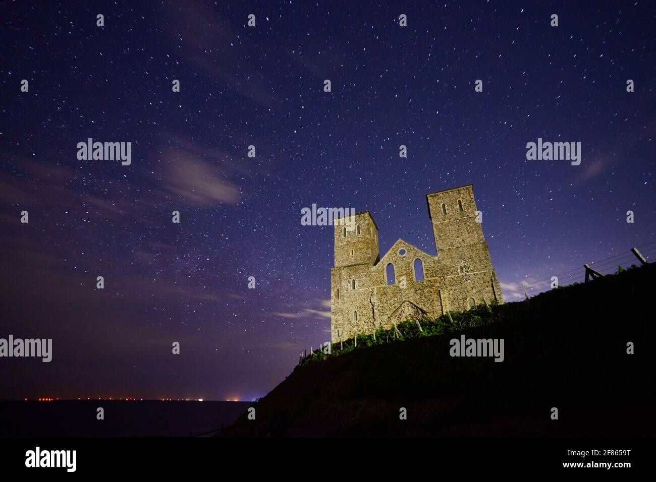 Reculver, Kent, UK. 12th April 2021: UK Weather. Clear skies with stars and a few clouds overnight of the 11th/12th April at the ruined church at Reculver, abandoned due to erosion by the sea in the early 19th century, its distinctive twin towers were saved as a navigation aid for ships. Wind farms and ships can be see on the horizon. Credit: Alan Payton/Alamy Live News Stock Photo