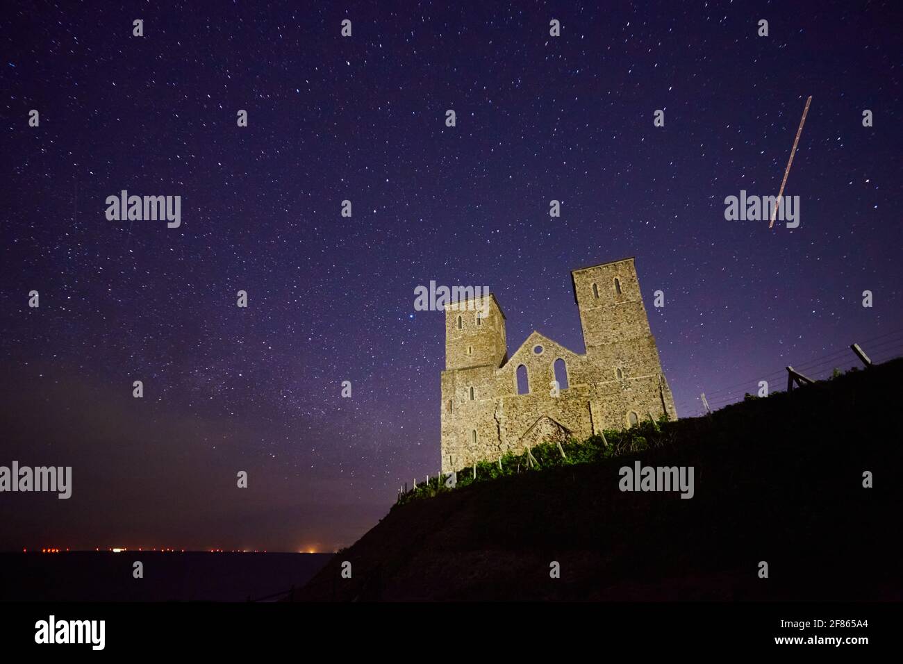 Reculver, Kent, UK. 12th April 2021: UK Weather. Clear skies with stars and a few clouds overnight of the 11th/12th April at the ruined church at Reculver, abandoned due to erosion by the sea in the early 19th century, its distinctive twin towers were saved as a navigation aid for ships. Wind farms and ships can be see on the horizon. A plane flies ovehead. Credit: Alan Payton/Alamy Live News Stock Photo