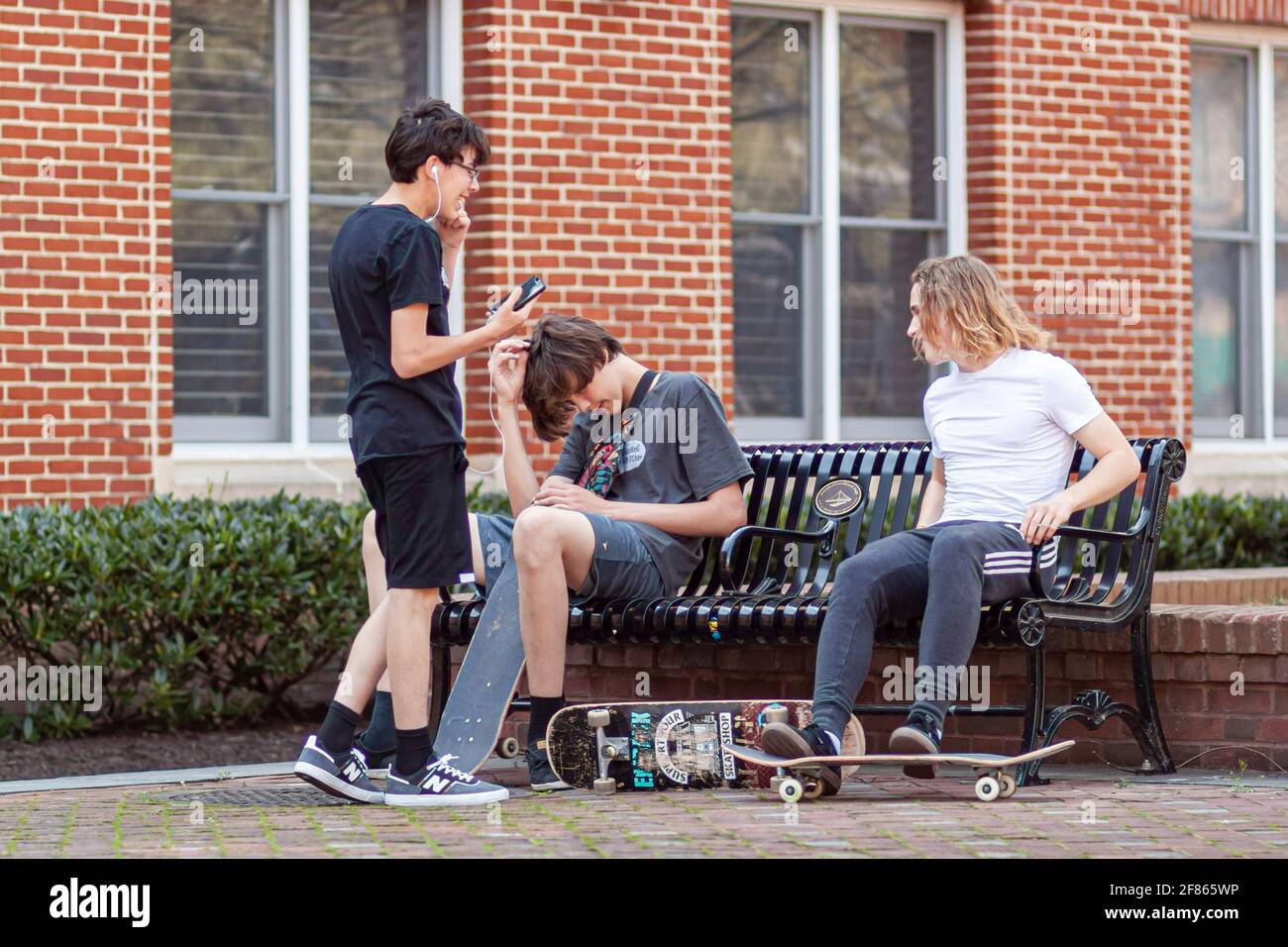 Frederick, MD, USA 04-07-2021: Three teenager boys wearing casual trendy clothes are hanging out in a city park on a sunny day. Concept image for gene Stock Photo