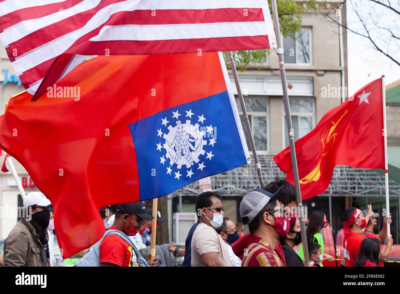 A protester carries the flag of the former Socialist Union of Burma upside down, a sign of distress, alongside an American flag and the flag of the Na Stock Photo